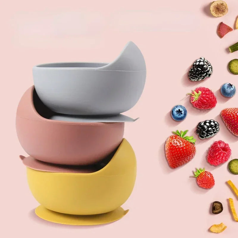 Stacked silicone baby bowls in pastel colors beside assorted fresh berries.