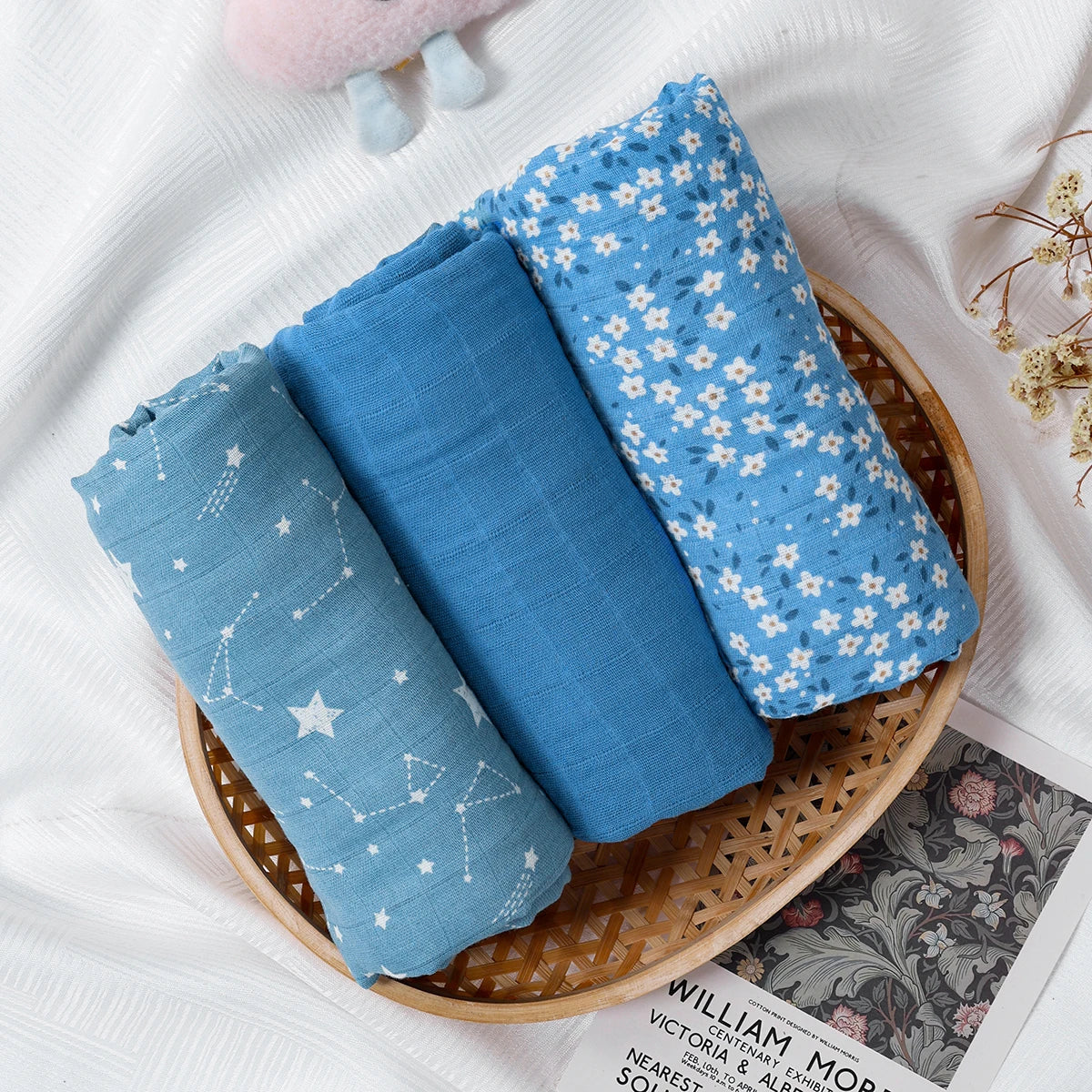 Three rolled blue baby swaddle blankets with star and floral patterns on a wicker tray