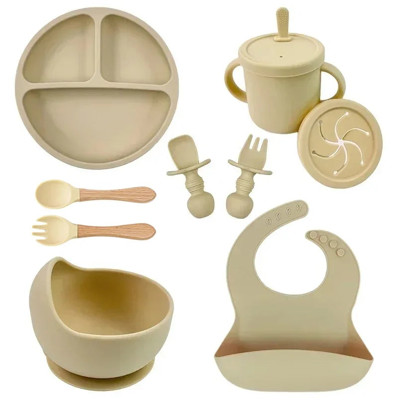 Beige silicone baby feeding set with bib, suction bowl, plate, utensils, cup, and snack lid