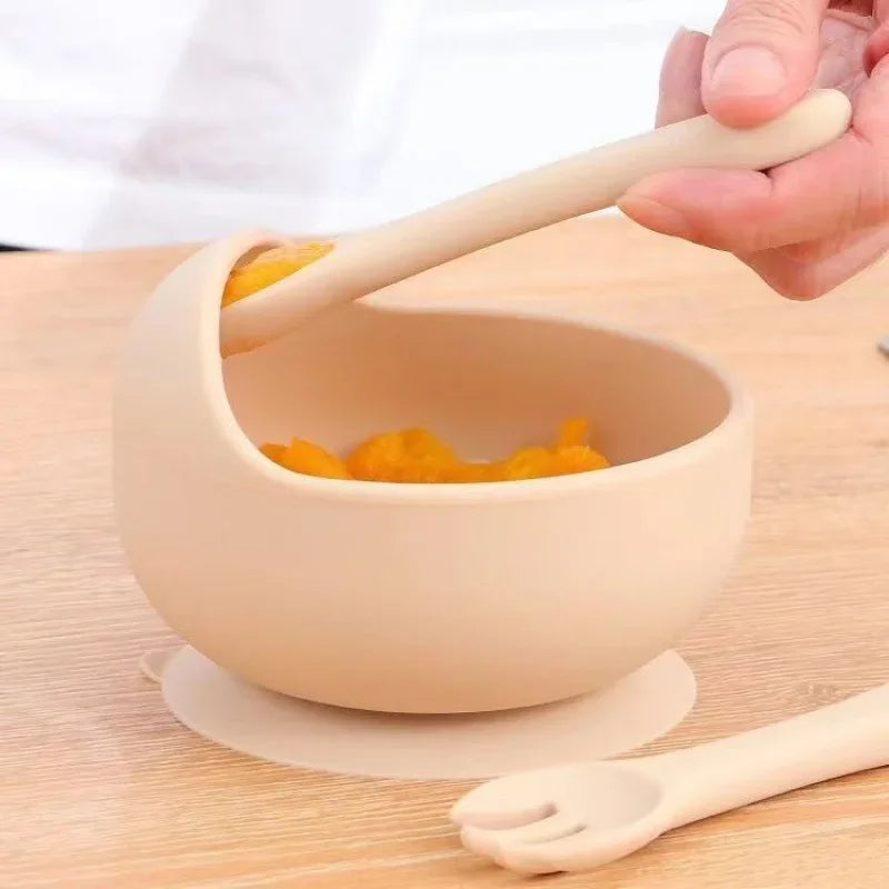 Hand scooping baby food from silicone suction bowl with spoon on wooden table