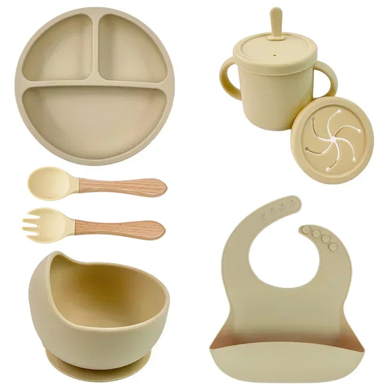 Beige silicone baby feeding set with plate, bowl, bib, cup, spoon, and fork.