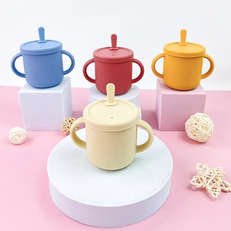 Four silicone baby sippy cups with handles and lids in pastel colors on display blocks
