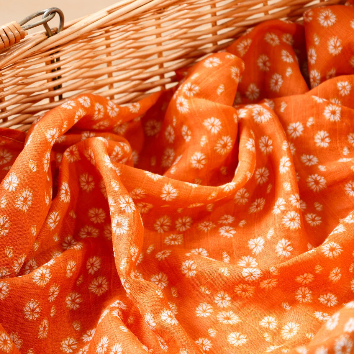 Orange muslin baby blanket with white floral pattern in wicker basket