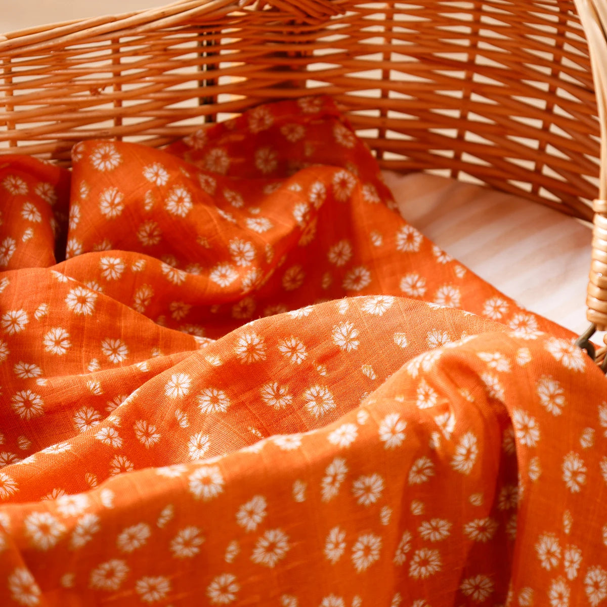 Orange floral muslin baby blanket in a wicker bassinet, soft and cozy newborn bedding