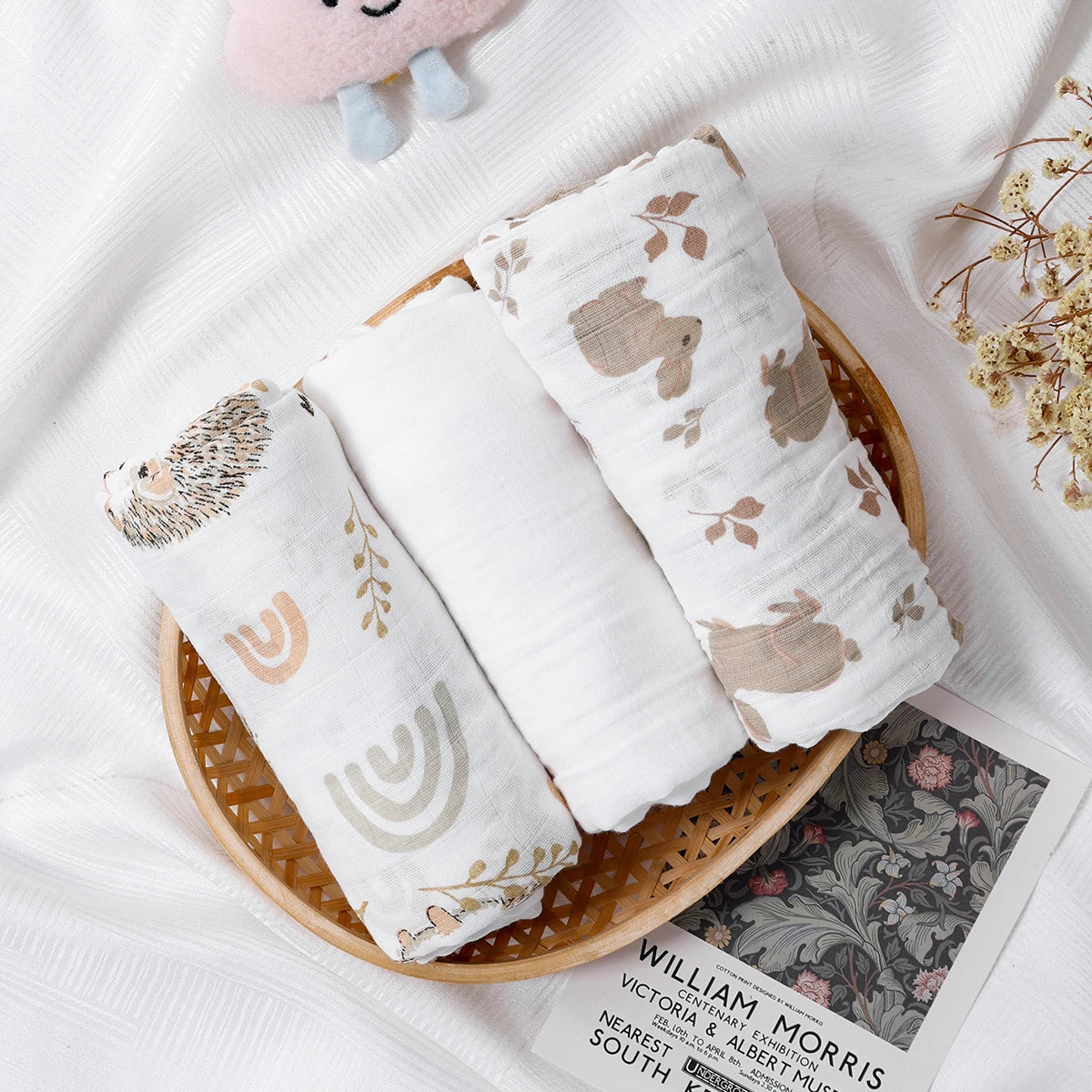 Three soft baby muslin swaddle blankets with cute animal and nature prints in a basket