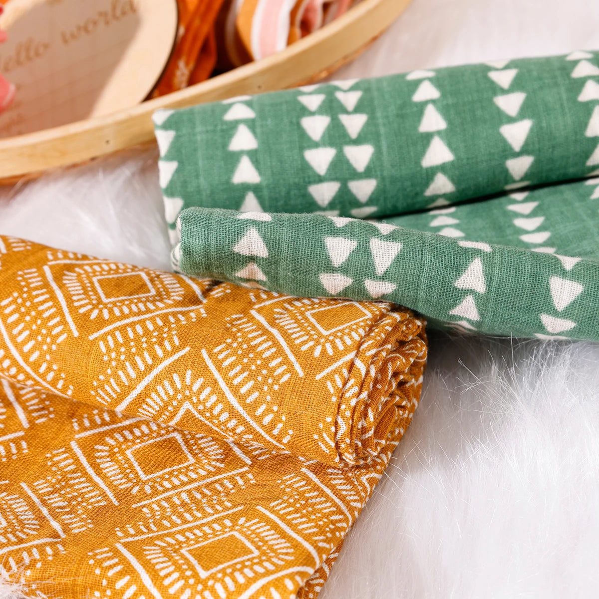Close-up of patterned baby muslin swaddle blankets in yellow and green on soft white fur