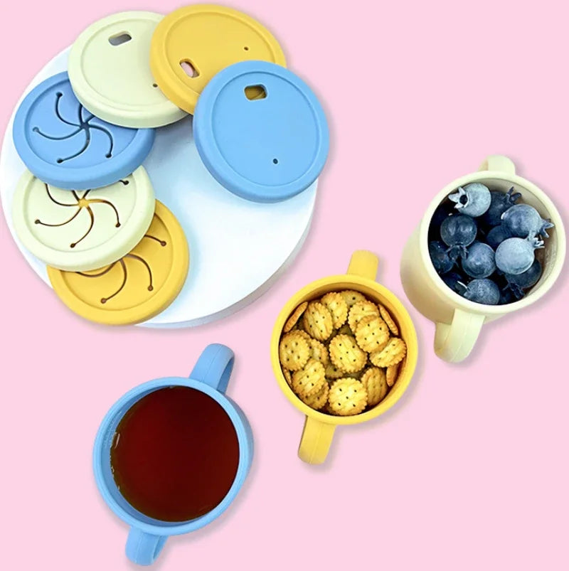 Colorful silicone toddler snack cups with lids, filled with juice, crackers, and blueberries.