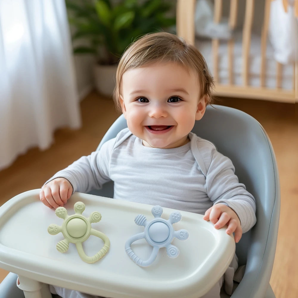 Smiling baby in high chair with two silicone teething toys on tray, nursery background