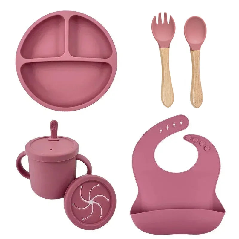 Pink silicone baby feeding set with bib, divided plate, snack cup, fork, and spoon